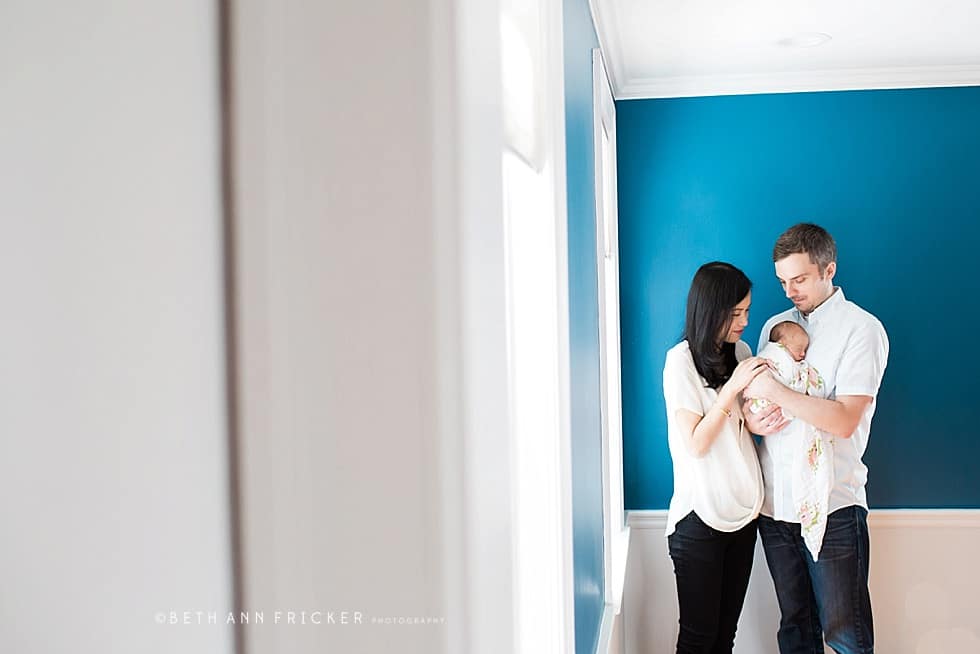newborn baby with mom and dad in front of blue wall boston newborn photographer