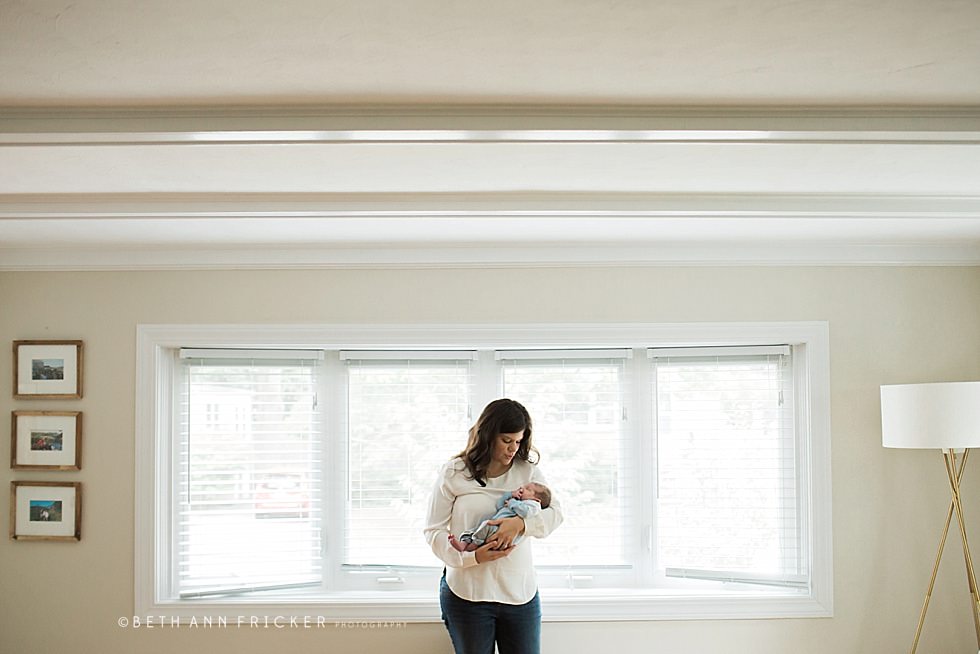 mom holding newborn in front of window reading MA newborn photographer