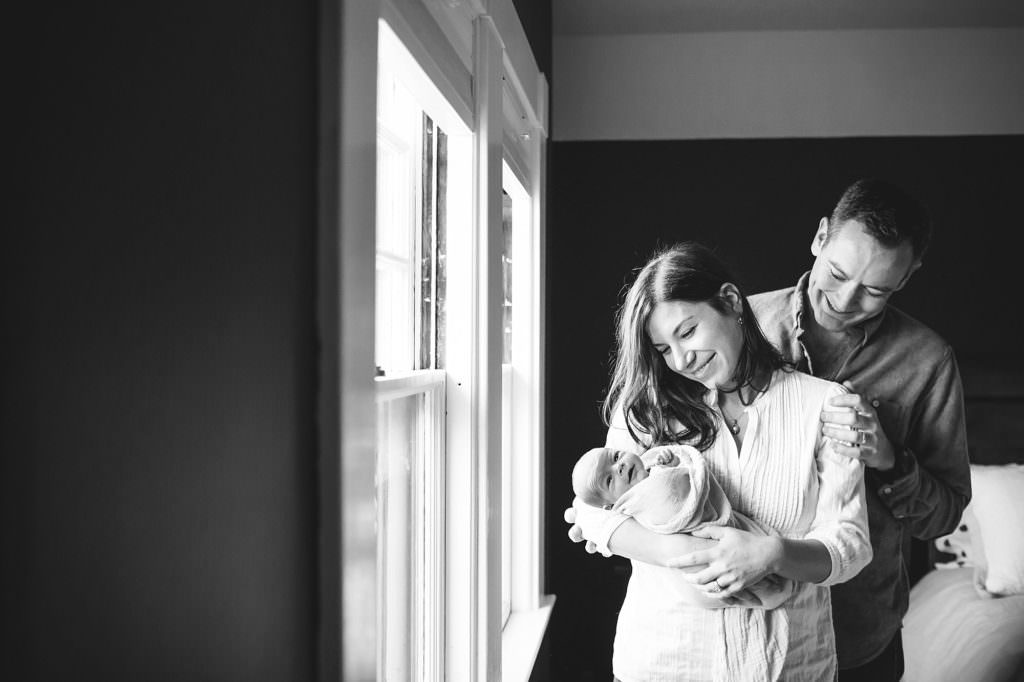 Mom and dad holding newborn baby daughter by the window black and white Boston Newborn Photographer