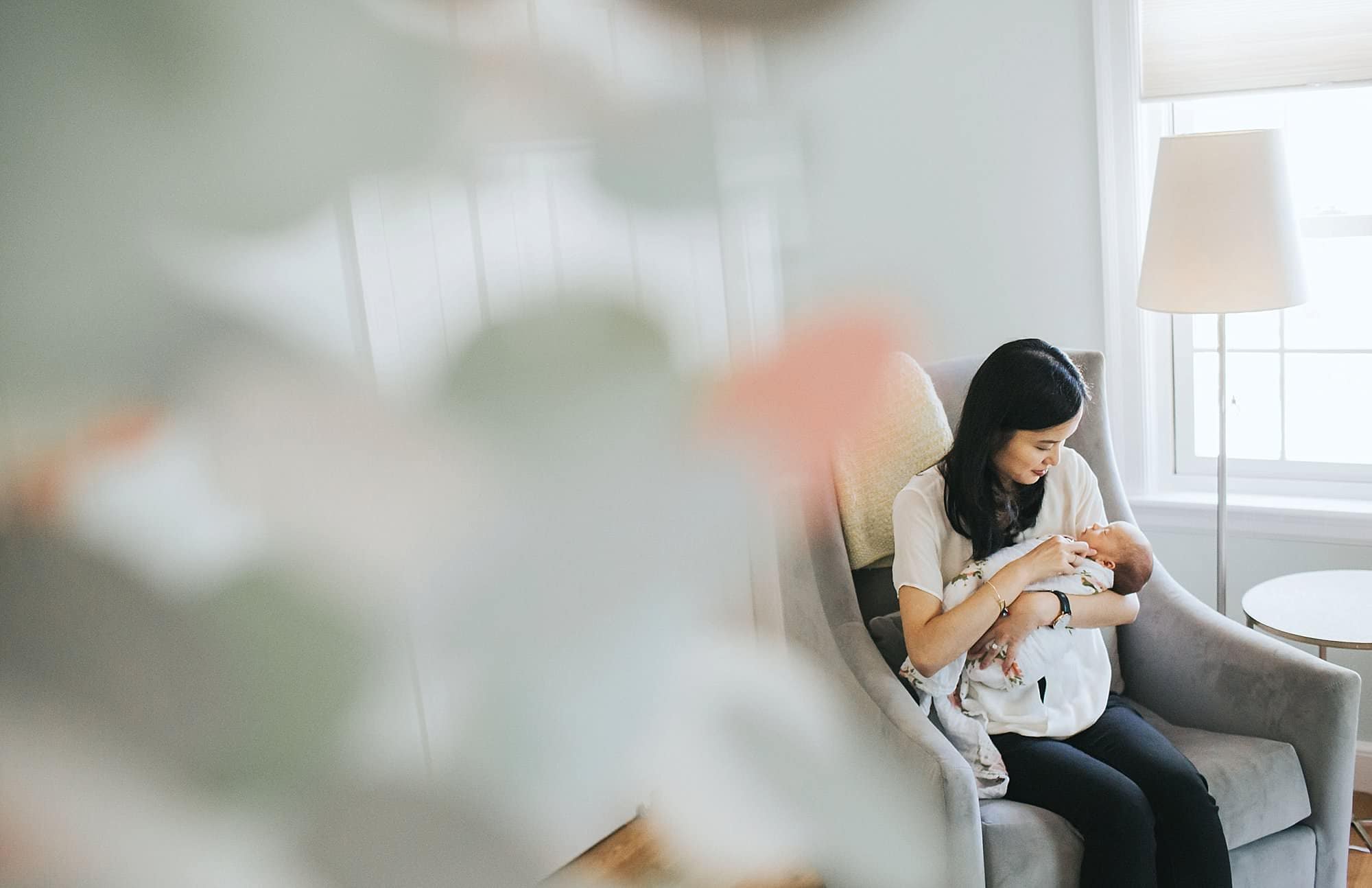 Mom sitting with newborn in nursery Boston baby photographer