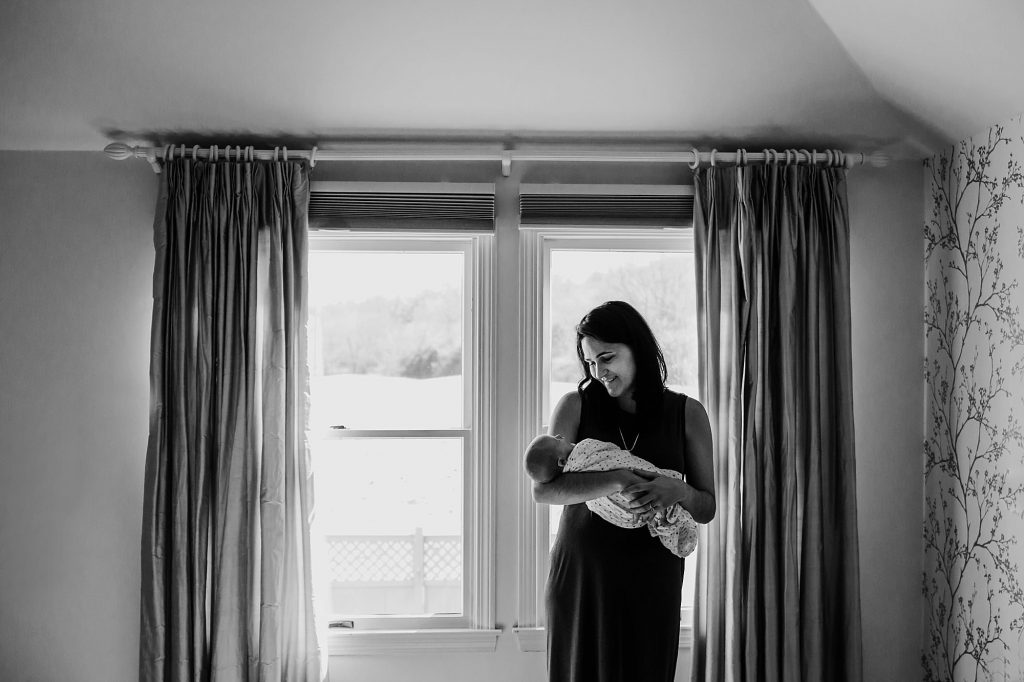 mom holding baby near the window Hingham newborn photographer