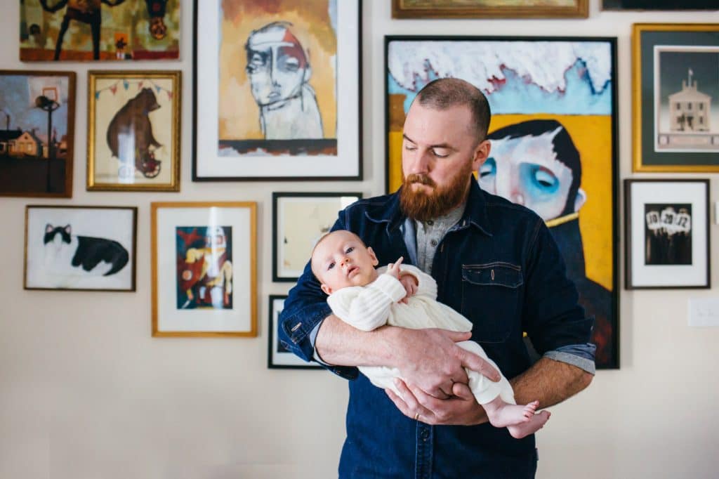 dad holding newborn in front of art