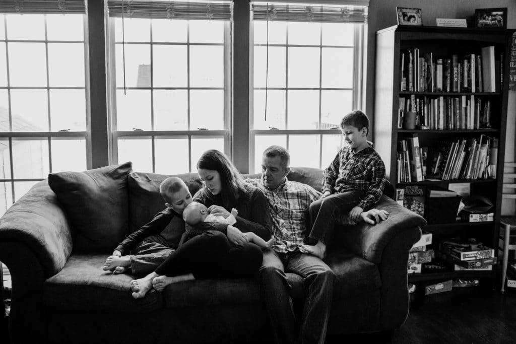 family with new baby sitting on couch rochester ny newborn photographer