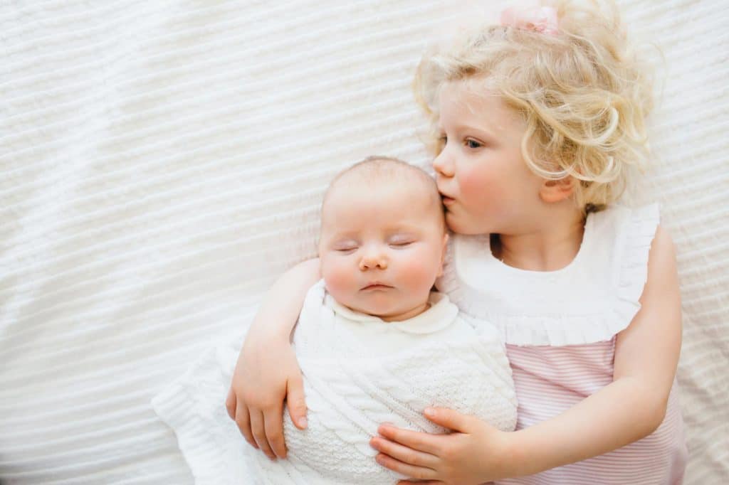 Big sister kissing baby sister belmont newborn photographer