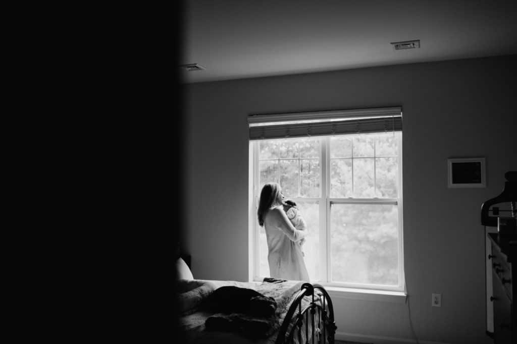 mom holding baby by window Concord newborn photography