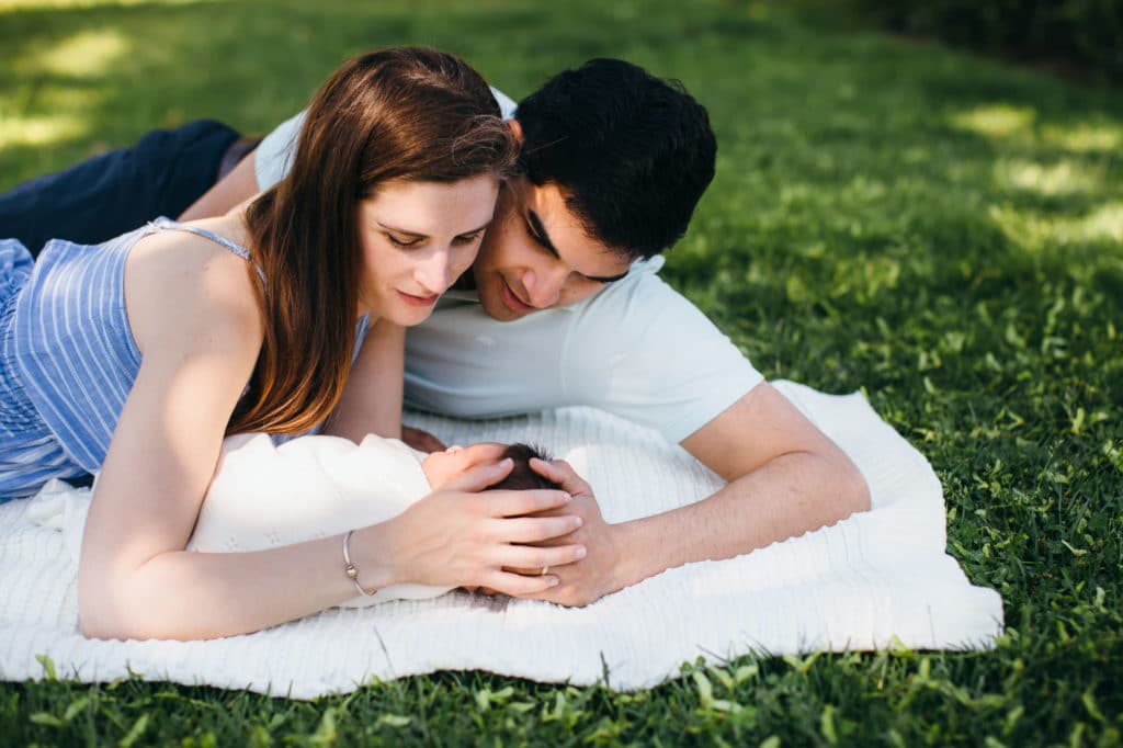 parents cuddling newborn laying in grass Boston baby photos