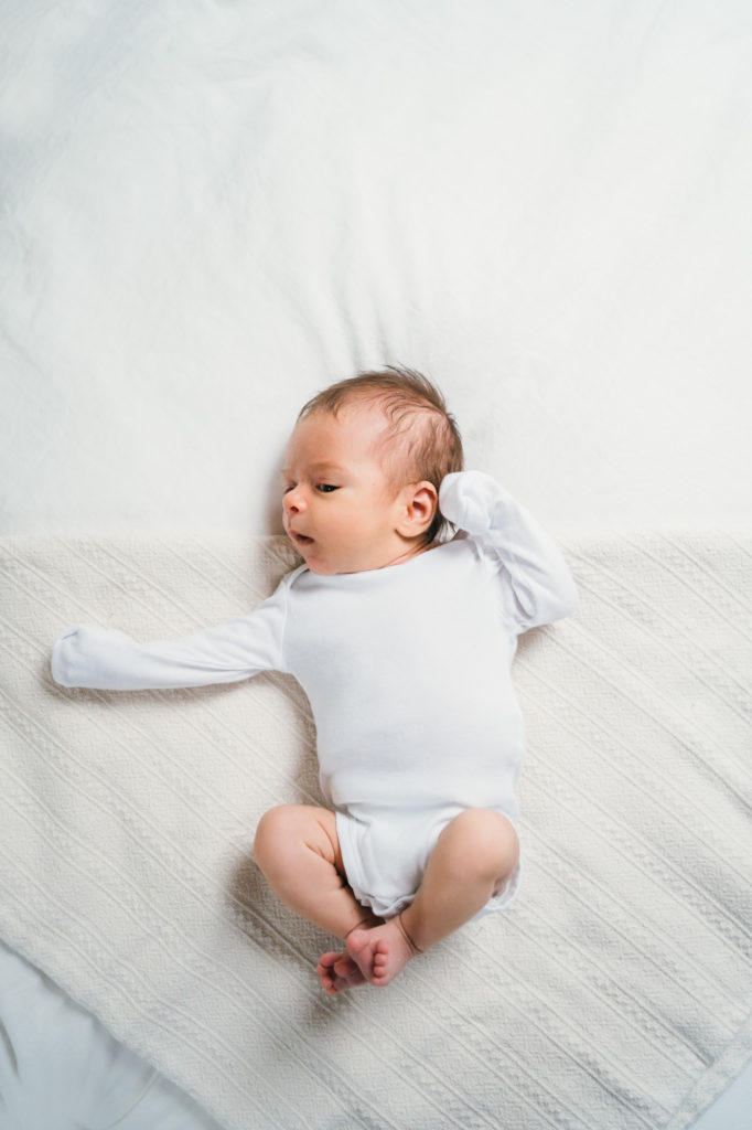 baby laying on bed in white onesie Arlington MA Photographer 